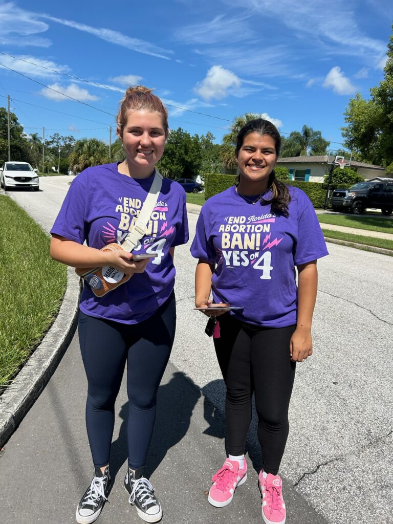 Two student volunteers wear purple shirts and smiles, advocating to end Florida's near-total abortion ban by inspiring voters to vote YES on Amendment 4